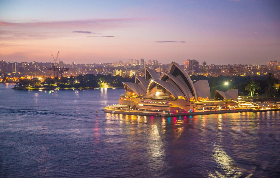 Sydney Opernhaus am Hafen von Sydney in Australien bei Tageslicht mit blauem Himmel und Wasser im Vordergrund.